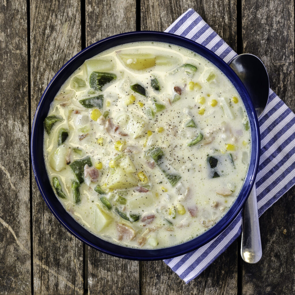 bowl of corn chowder in a blue bowl on top of a blue and white striped napkin and a wood table.
