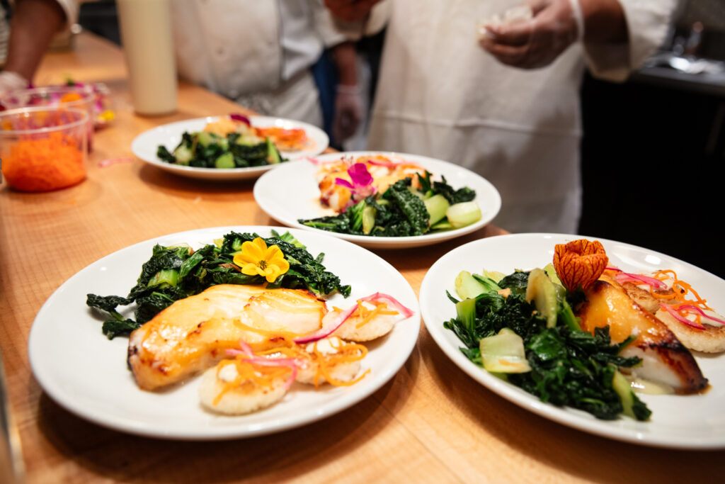 four dinner plates with fish, rice cakes, and greens